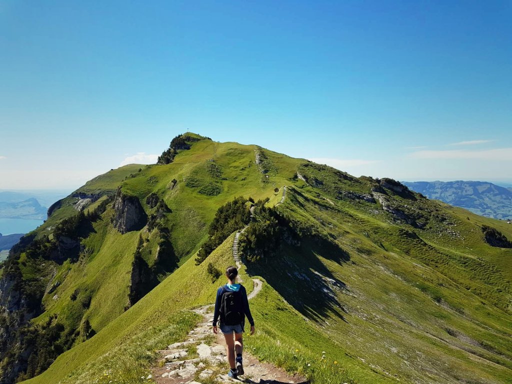 Wanderin auf einem gruenen Bergweg mit Blick auf die Berge